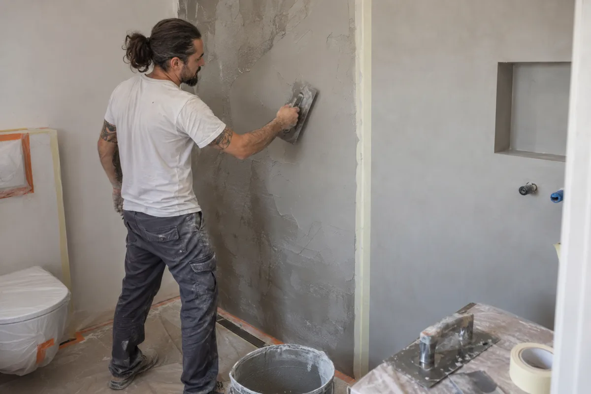 Aplicador extendiendo microcemento gris con llana en la pared de un baño en obra
